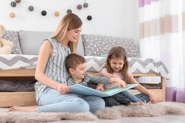 Nanny reading book to little children at home - Foto, Imagen