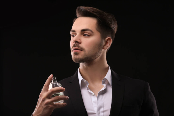 Handsome man in suit using perfume on black background - Photo, image