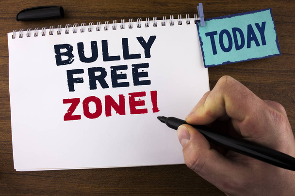 Handwriting text writing Bully Free Zone Motivational Call. Concept meaning creating abuse free school college life written by Man on Notepad holding Marker on wooden background Today Clip. - Photo, Image