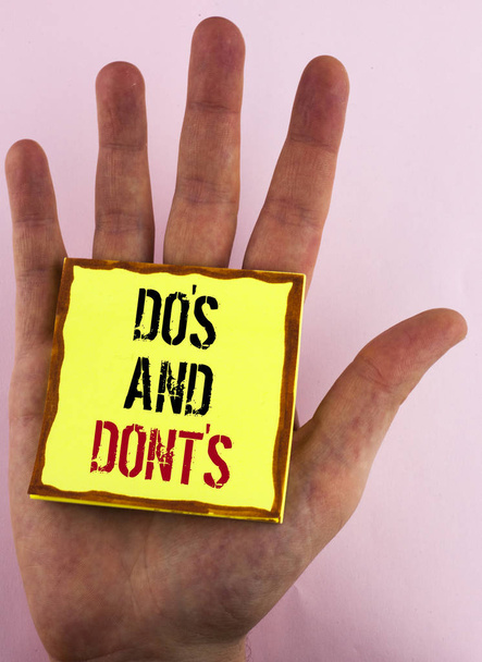 Signo de texto que muestra Do 'S y Don' t. Foto conceptual Qué se puede hacer y qué no se puede saber correcto mal escrito en Yellow Sticky Note Papel colocado en la mano sobre el fondo liso
. - Foto, Imagen