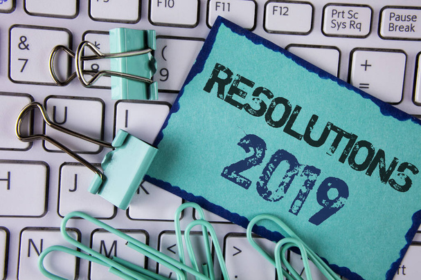 Handwriting text Resolutions 2019. Concept meaning Positive reinforcement personal improvent corporate goals written on Sticky Note paper placed on White Keyboard Clips and Paper Pins next to it. - Photo, Image