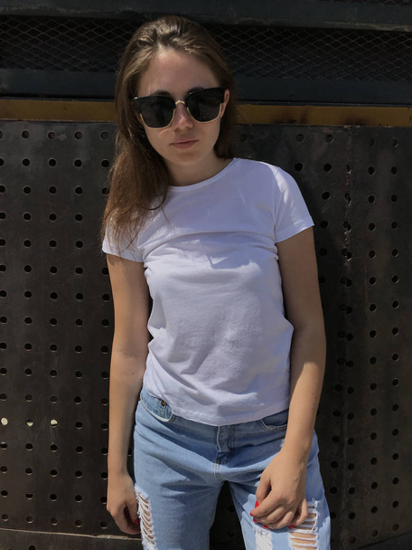 Attractive girl in a white t-shirt is standing on a metal background. - Foto, Imagen