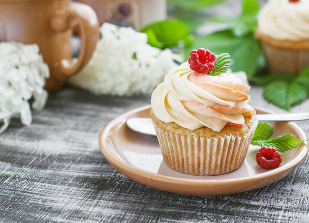 Delicate vanilla cupcakes with cream and raspberries on a dark wooden background - Photo, Image