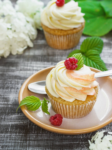 Delicate vanilla cupcakes with cream and raspberries on a dark wooden background - Foto, Bild
