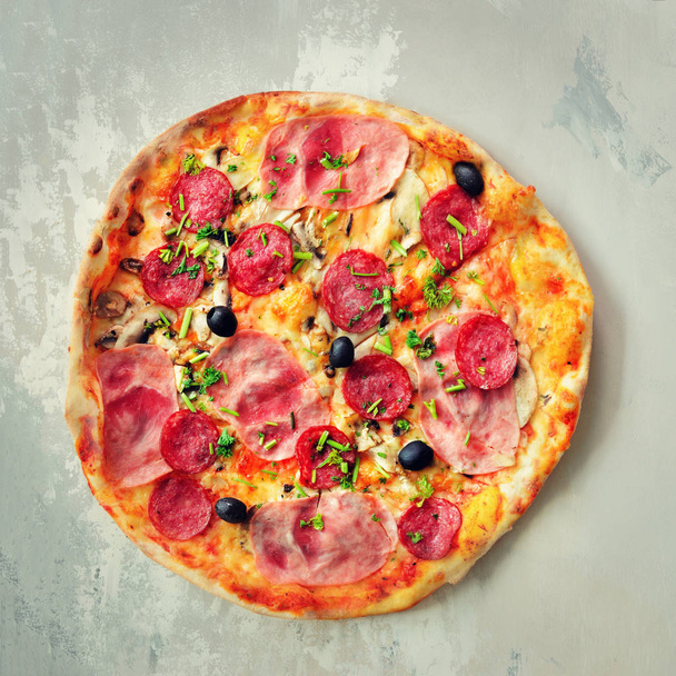 Fresh italian pizza with mushrooms, ham, tomatoes, cheese, olive, pepper on grey concrete background. Copy space. Top view. Square crop - Foto, Bild
