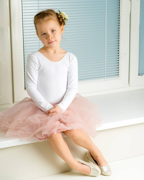 A little girl is sitting by the window with jalousie - Foto, Imagen