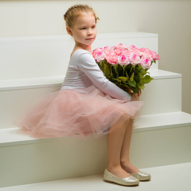 Little girl with a bouquet of flowers sits on a white staircase. - Fotografie, Obrázek