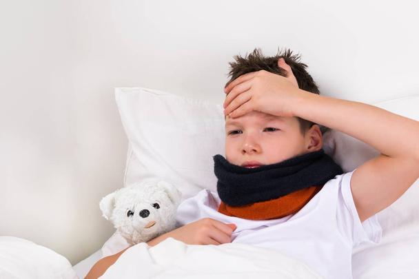Junge mit Teddybär liegt mit Fieber im Bett - Foto, Bild