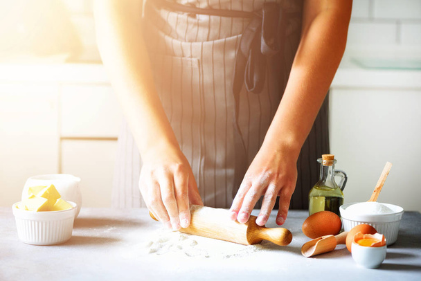 Female hands kneading dough, baking background. Cooking ingredients - eggs, flour, sugar, butter, milk, rolling pin on white style kitchen. Copy space - Zdjęcie, obraz