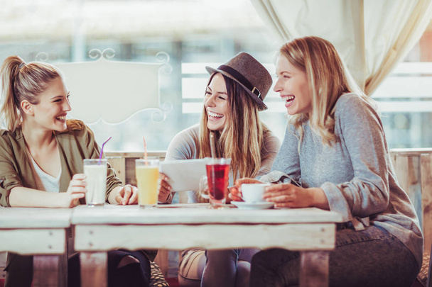 Θηλυκό φίλους απολαμβάνοντας συνομιλία και πίνοντας τον καφέ στην καφετέρια και χρησιμοποιώντας ψηφιακό tablet. - Φωτογραφία, εικόνα