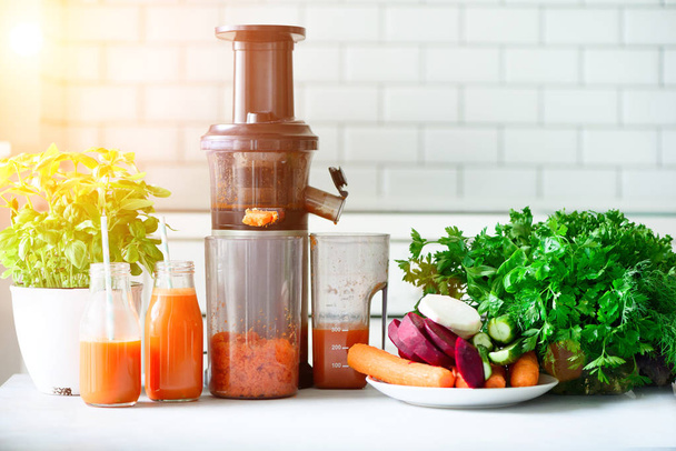 Woman making fresh drink. Juicer and carrot juice. Fruits in background. Clean eating, detox concept. Sunny morning with sunlight. Toned effect - Photo, Image