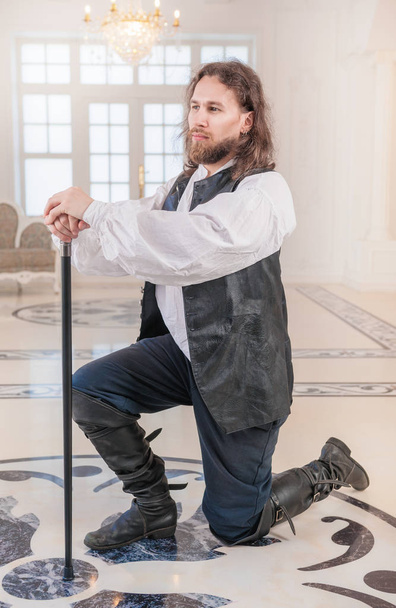 Odważny człowiek w średniowiecznych ubraniach z trzciny stojący na kolana - Zdjęcie, obraz