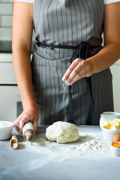 Female hands kneading dough, baking background. Cooking ingredients - eggs, flour, sugar, butter, milk, rolling pin on white style kitchen. Copy space - Фото, изображение