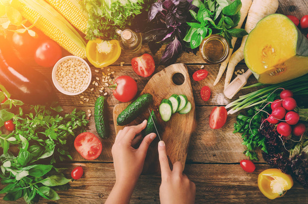Woman hands cutting vegetables on wooden background. Vegetables cooking ingredients, top view, copy space, flat lay. Sunlight bokeh - 写真・画像