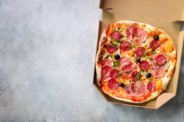 Fresh pizza in delivery box on grey concrete background. Top view, copy space - Foto, afbeelding