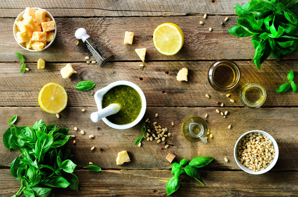 Ingredients for homemade pesto - basil, lemon, parmesan, pine nuts, garlic, olive oil and salt on rustic wooden background. Top view, flat lay, copyspace - Photo, image