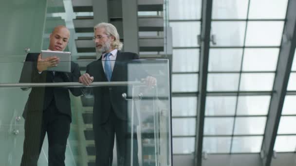 dva firemních manažerů stojící na druhém patře na skla a oceli budování diskutovat podnikání pomocí digitálních tabletu. - Záběry, video