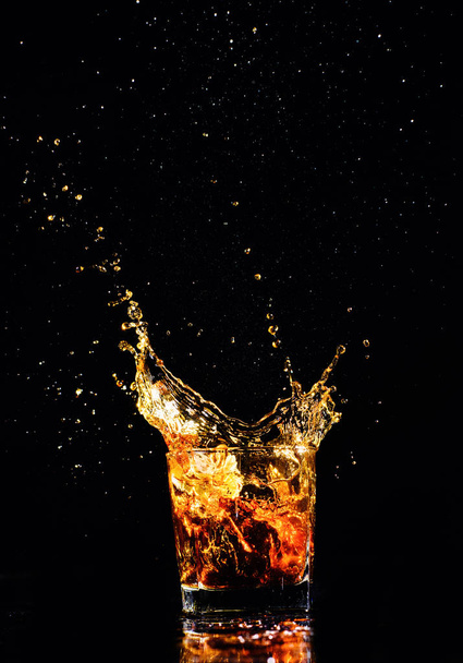 Isolated shot of whiskey with splash on black background, brandy in a glass - Foto, afbeelding
