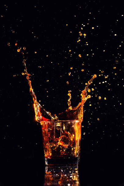 Isolated shot of whiskey with splash on black background, brandy in a glass - Photo, image