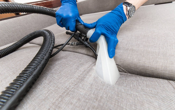 Cleaning service. Man janitor in gloves and uniform vacuum clean sofa with professional equipment - Fotoğraf, Görsel