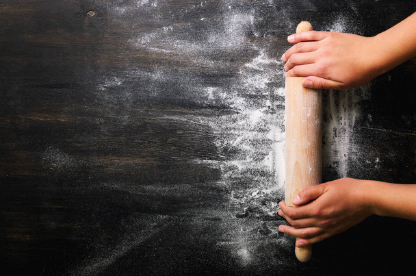 Girl hands keep rolling pin with flour on dark black table, baking background, top view, copy space for your text, meru, recipe. Banner - Valokuva, kuva