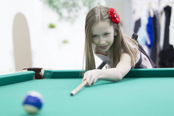 Ein Teenager-Mädchen spielt Billard. interessantes Spiel. Eine nützliche Lektion für ein Kind - Foto, Bild