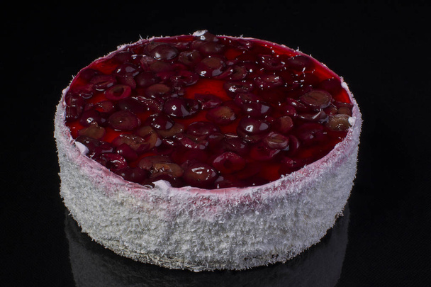 Big cake in coconut shavings with a cherry in jelly on a black background - Foto, Bild