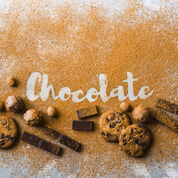 Слово шоколад, напечатанный на какао на сером фоне среди какао и шоколадного печенья, кусочки шоколада, орехи в шоколаде и сладости. Я люблю шоколад
 - Фото, изображение