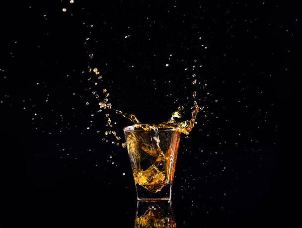Isolated shot of whiskey with splash on black background, brandy in a glass - Fotó, kép