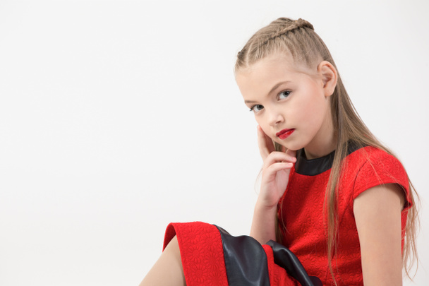 A teenaged blond girl in a red dress and brightly red lips on a white background.Portrait of a schoolgirl - Foto, Imagen