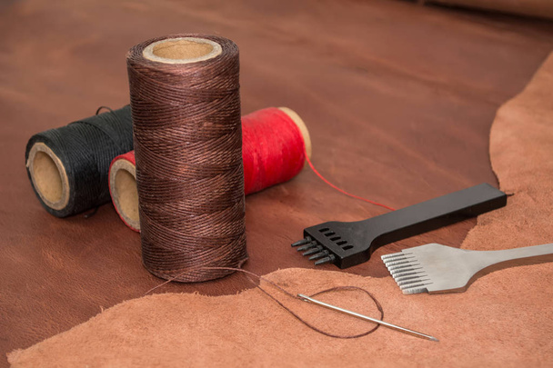 Outils pour l'artisanat du cuir, fil de cire avec une aiguille et des morceaux de cuir brun
 - Photo, image