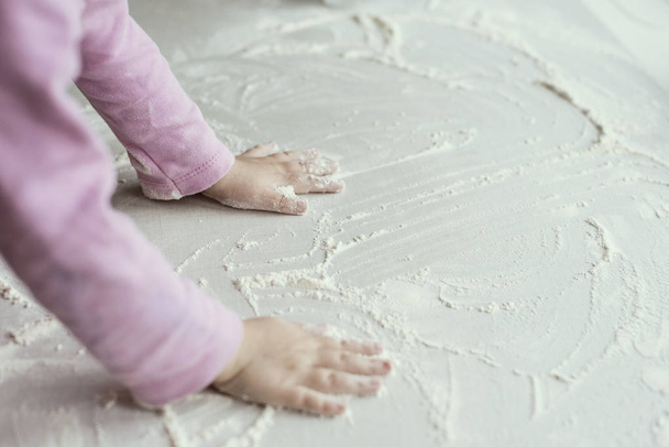 La niña está jugando en la cocina, con las manos en la harina
 - Foto, Imagen