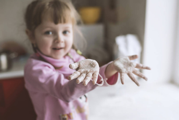 Pikkutyttö leikkii keittiössä, kädet jauhoissa.
 - Valokuva, kuva