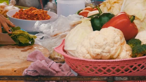 Nainen leikkaa vihanneksia keittiön laudalla suurella veitsellä lähikuva. Vihannesten ja keittiövälineiden vieressä. Thai katu ruoka
 - Materiaali, video