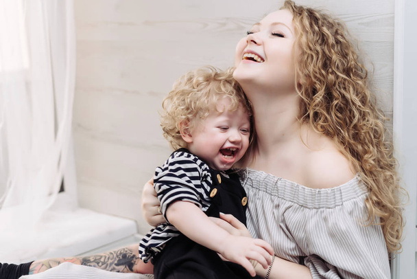 happy friendly family, a young curly mother holding her little son in her arms, laughing and playing - Photo, Image