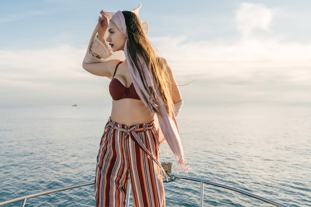 stylish long-haired girl is standing on her white yacht in the sun, sailing to the Caribbean islands on vacation - Photo, Image