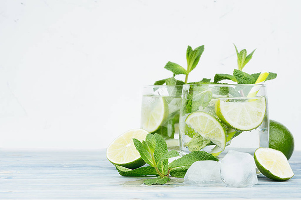 Tropical fresh cold cocktail gin tonic with mint, lime, ice, straw on light blue shabby wood board and white background, copy space. - Фото, изображение