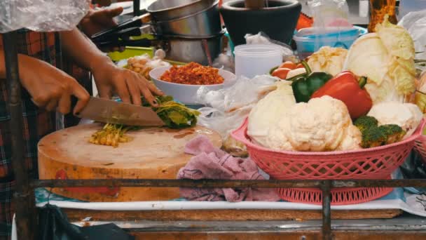 女性は、大きなナイフでキッチン ボードに緑をカットします。野菜や調理器具に次へ。タイの屋台 - 映像、動画