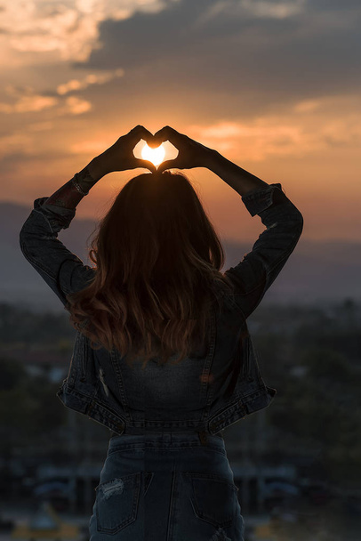 femme faisant une forme de coeur avec ses mains contre la lumière de su
 - Photo, image