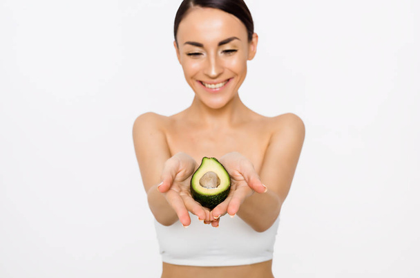 Avocado for a healthy body. A beautiful young girl holds half the avocados in her hands and points to the camera. - Foto, immagini