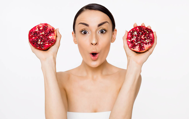 Bright and emotional beautiful woman with half a pomegranate in hands posing in front of the camera. Fruit is health. - Zdjęcie, obraz