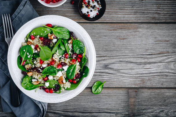 grüne Salatspinatschüssel mit Quinoa, Granatapfel, Walnüssen, Feta-Käse und getrockneten Preiselbeeren.  - Foto, Bild