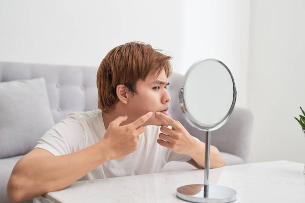 asiático hombre mirando espejo y popping espinilla
 - Foto, Imagen