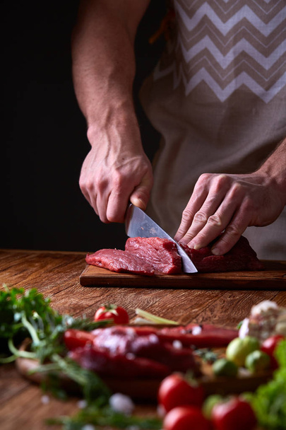 Strong professional mans hands cutting raw beefsteak, selective focus, close-up - Fotó, kép
