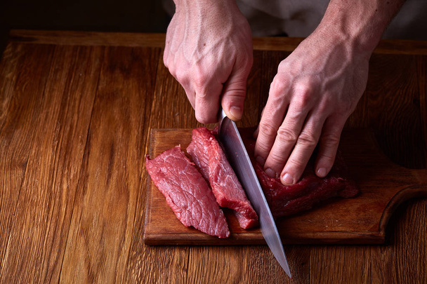 Strong professional mans hands cutting raw beefsteak, selective focus, close-up - Фото, зображення