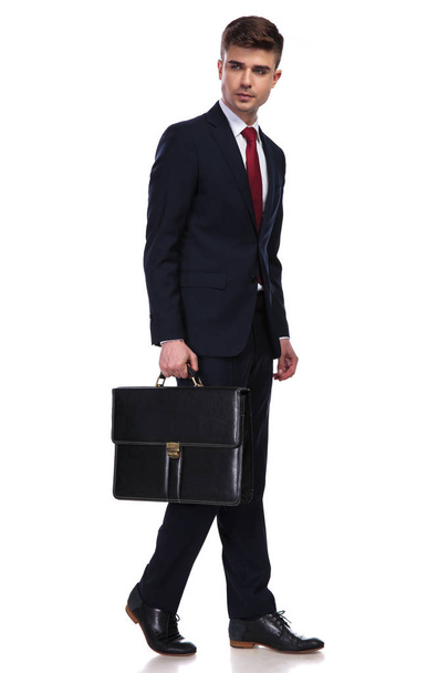 walking businessman looks to side while holding a suitcase - Photo, Image