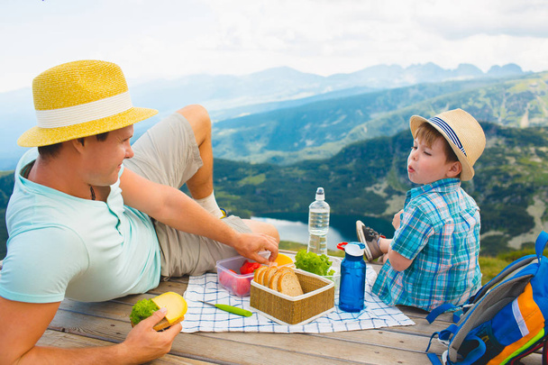 Father and son eat healthy sandwiches on a picnic in the mountains. Rila Lakes in Bulgaria. - Zdjęcie, obraz