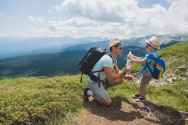 Father and son hiking in Rila mountains, Bulgaria. dad giving water to his son. - 写真・画像