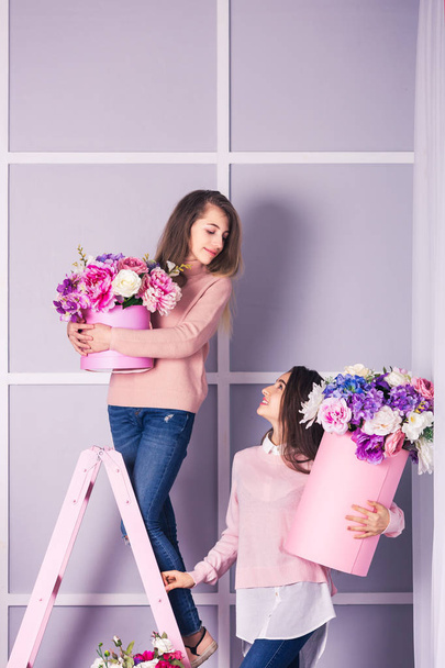 Две красивые девушки в джинсах и розовый свитер в студии с декором цветов в корзинах
. - Фото, изображение
