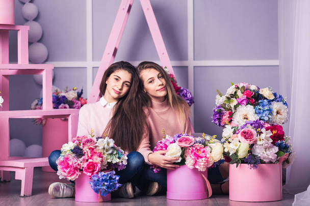 Дві красиві дівчата в джинсах і рожевий светр в студії з декором квітів в кошиках
. - Фото, зображення